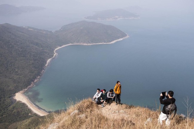 A man (R) takes a photo of fellow hikers on top of Sharp Peak overlooking a bay in Sai Kung Country Park, Hong Kong on December 29, 2013. The World Wildlife Fund (WWF) along with 20 other groups formed in 2013 a coalition to lobby the Hong Kong government to protect the southern Chinese territory's 24 designated country parks from business interests seeking to use parts of the land for housing purposes. AFP PHOTO / ALEX OGLE / AFP / Alex Ogle
